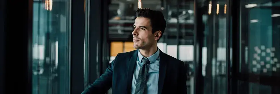 Young well-dressed businessman standing in a modern office space walkway staring out of window