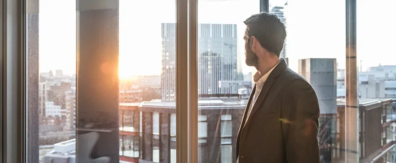 Businessman staring out of office window at sundown