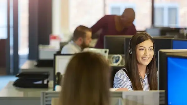 Young female IT Support Agent smiling at digital display in a busy office