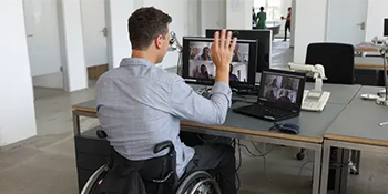 Man sitting at desk in wheelchair waving at people on a video call