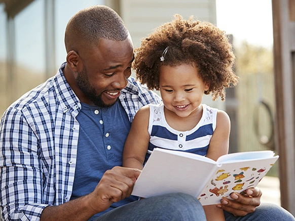 Parent and child seated outside reading a book together