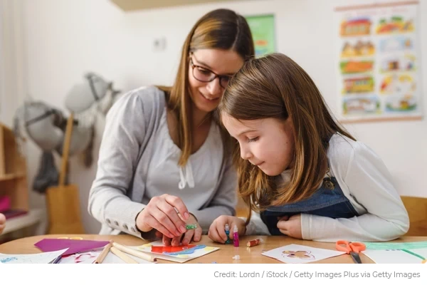 Mother and daughter seated in learning environment engaged in craft activity