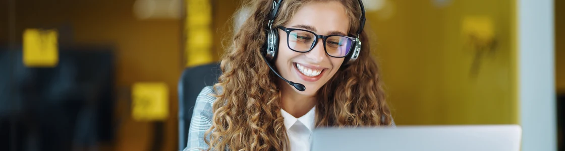 Young IT Service professional using a VoIP headset to communicate with a customer while seated in a modern office environment