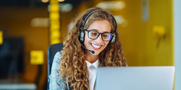 Young IT Service professional using a VoIP headset to communicate with a customer while seated in a modern office environment