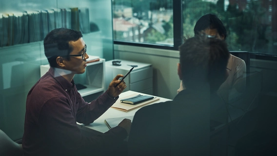 Business professionals in discussion whilst seated in a dimly lit modern office space with large windows