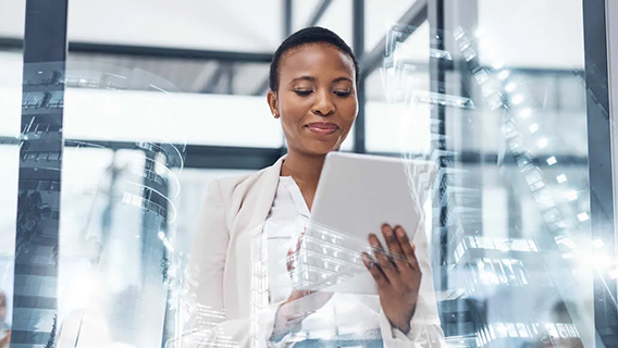 Well-dressed female executive standing in brightly-lit modern office space while smiling and using a digital tablet device