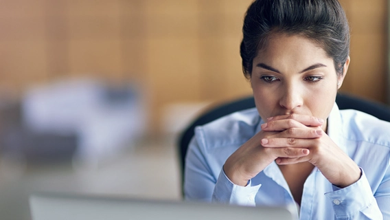 Concerned-looking businesswoman seated while staring at a laptop screen alongside her