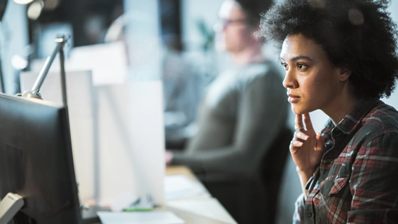 Young professional looking worriedly at a monitor screen while seated at her desk in a modern office environment