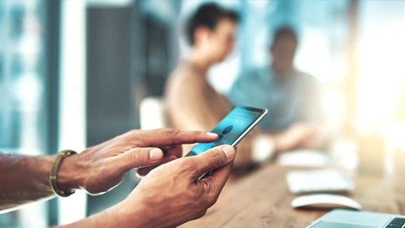 Close-up image of two hands using a mobile device in a modern office space