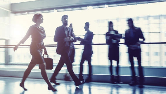 Well-dressed businesspeople moving quickly through a modern brightly-lit glass building