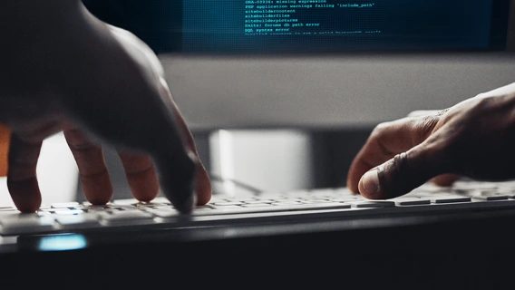 Close-up shot of mans' hands using a keyboard in front of a desktop monitor