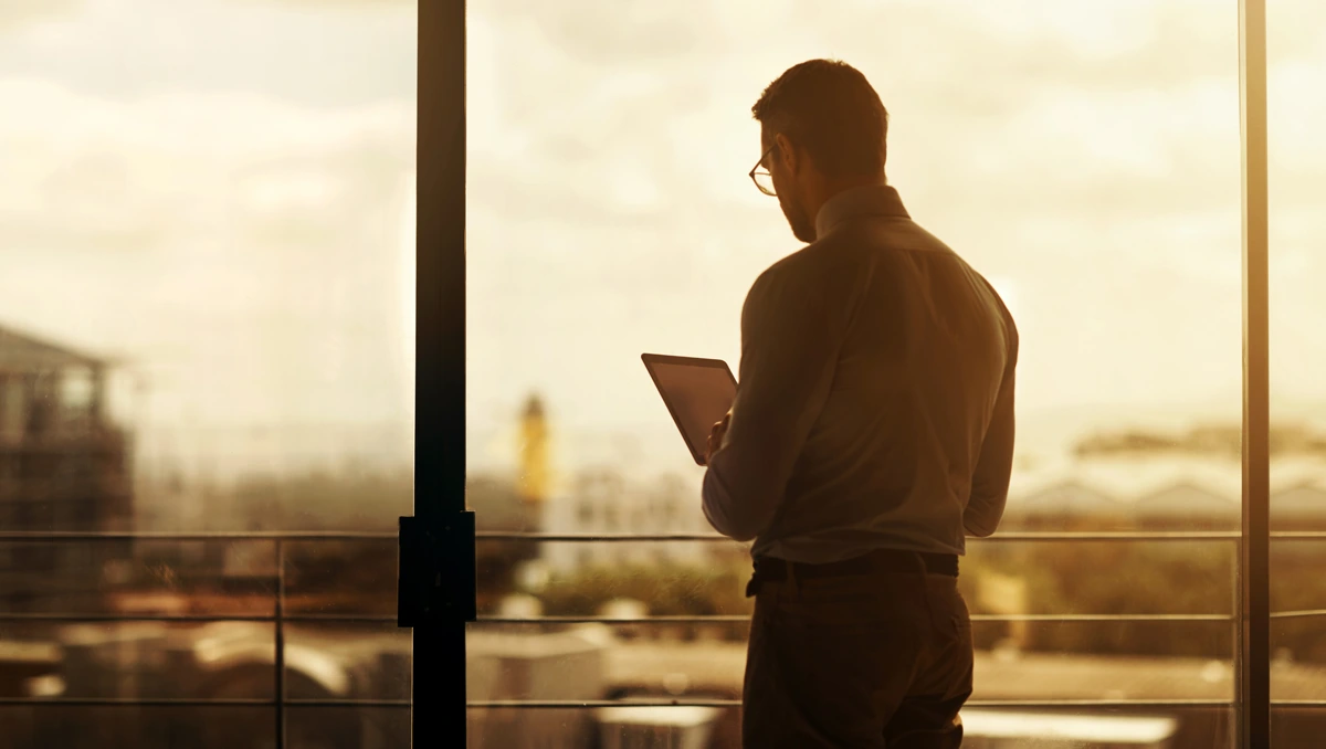 Business professional standing in a modern office environment before a large window using a tablet device