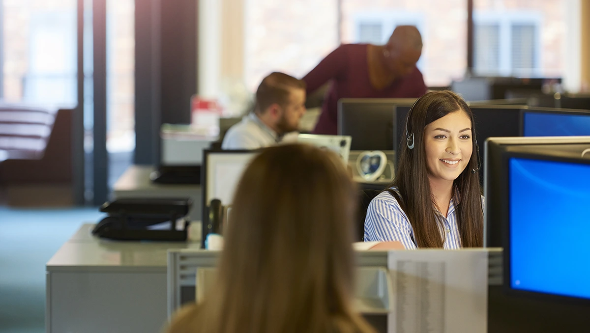 Staff seated in an office environment with focus on a smiling your IT professional using a headset
