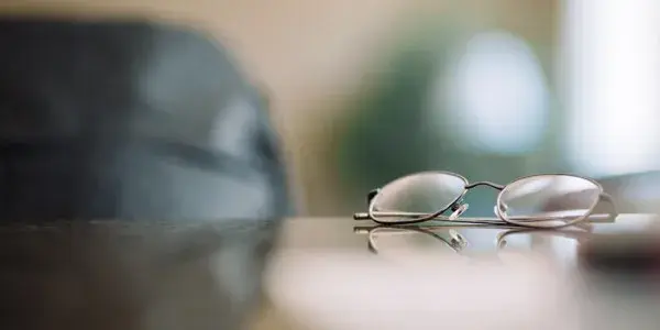 Defocused shot of glasses on office desk with chair in distance
