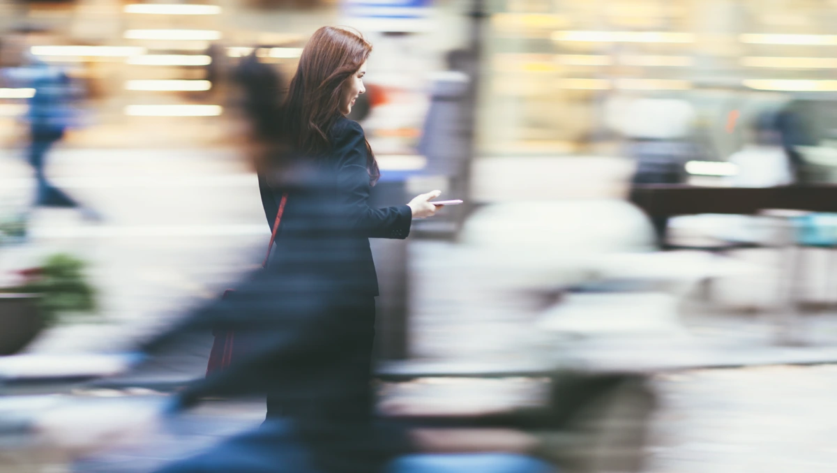 Motion shot of young professional walking on the street holding a mobile device